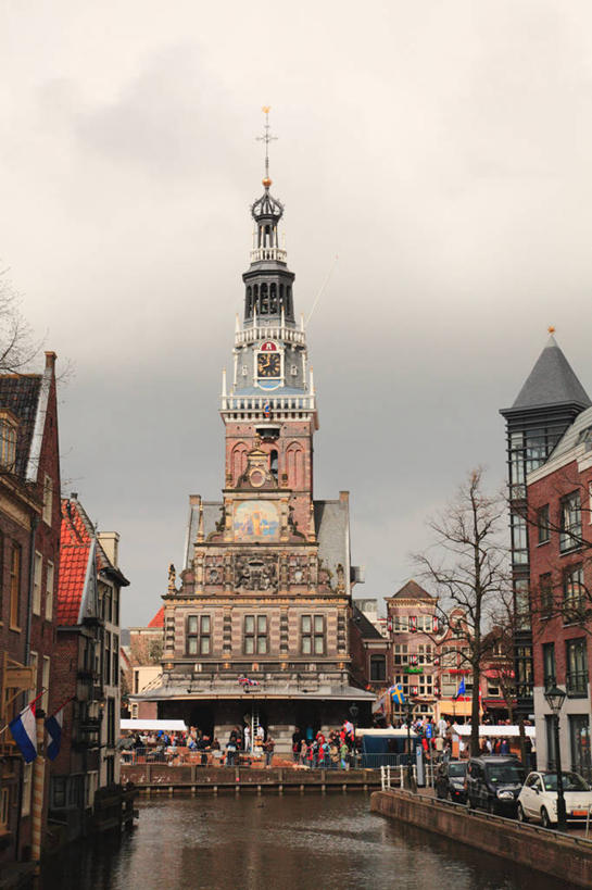 西方人,背部,家,栏杆,站,坐,走,竖图,室外,白天,正面,旅游,度假,河流,水,植物,标志建筑,地标,建筑,旗帜,欧洲,荷兰,欧洲人,行人,游客,游人,阴影,服装,时间,光线,时钟,影子,房屋,屋子,河水,水流,云,云朵,围栏,钟楼,首都,许多人,计时,云彩,注视,休闲装,娱乐,旗子,建设,护栏,楼房,路人,旅客,住宅,树,树木,衣服,蓝色,绿色,白云,蓝天,天空,阳光,自然,钟表,天,观察,看,站着,一群人,享受,休闲,休闲服,表,旅游胜地,放松,服饰,生长,晴朗,成长,观看,察看,西欧,关注,阿姆斯特丹,塔钟,旌旗,旗号,荷兰王国,尼德兰王国,过客,北荷兰省,阿克马,男人,男性,年轻男性,年轻女性,女人,女性,白种人,钟,晴空,步行,散步,站立,走路,坐着,半身,彩图,房子