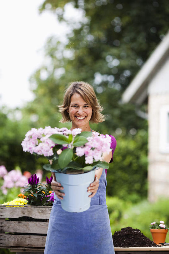 西方人,一个人,家,站,捧,笑,微笑,露齿笑,竖图,室外,白天,正面,植物,椅子,花盆,欧洲,欧洲人,仅一个女性,仅一个人,阴影,服装,朦胧,模糊,盛开,光线,围裙,影子,长椅,房屋,木椅,屋子,园艺,棕色,花蕾,注视,休闲装,楼房,住宅,花,花瓣,花朵,鲜花,树,树木,衣服,蓝色,绿色,紫色,阳光,自然,花苞,花蕊,观察,看,站着,仅一个中年女性,休闲,休闲服,服饰,生长,成长,观看,察看,关注,女人,女性,中年女性,白种人,卷发,端,端着,捧着,手捧,站立,半身,彩图,房子,短发