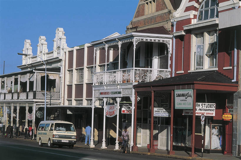 西方人,成年人,人群,栏杆,横图,室外,白天,太阳,城市,建筑,路,路灯,自行车,汽车,欧洲,非洲,津巴布韦,黑人,欧洲人,阴影,朦胧,模糊,标志,文字,柱子,机动车,首都,许多人,图像,车,脚踏车,天空,交通工具,一群人,概念,运输,摄影,英文字母,年龄,人造,照明设备,载具,主题,万里无云,构图,哈拉雷,男人,男性,女人,女性,非洲人,彩图,旅行,时空